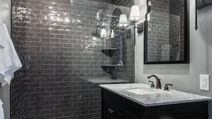 A modern bathroom with dark brick walls, a marble sink, and a large mirror. - Blacksmith Apartment | Lux Extended Stay in Belmont (Charlottesville)
