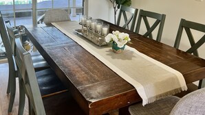A dining area with a wooden table, chairs, a hanging light fixture, a vase with flowers, and a painting on the wall.