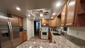 A kitchen with granite countertops, stainless steel appliances, wooden cabinets, and a ceiling fan.