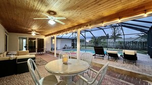 An outdoor patio with a round table and chairs, a ceiling fan, and a view of a swimming pool.