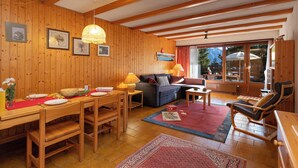 A wooden interior with a dining table, sofa, and chairs, a lamp, and a view through a glass door. - Centaure B RI 1 by Interhome (Ovronnaz)