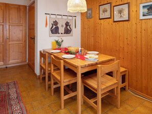 A wooden dining table with chairs, a red placemat, plates, a bowl of soup, and a vase with flowers.