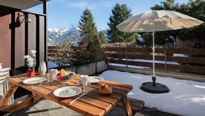 A wooden table set outdoors with plates, cutlery, a bowl of fruit, and a teapot. - Centaure B RI 1 by Interhome (Ovronnaz)