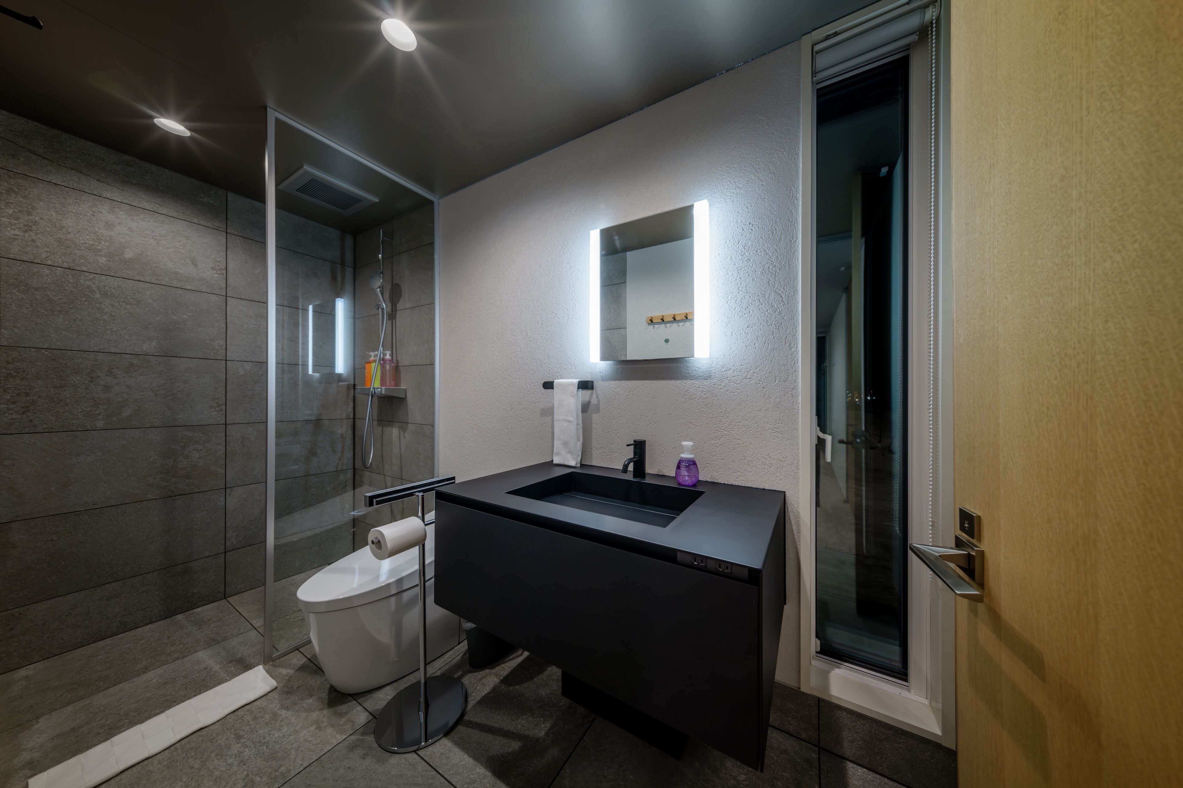 A modern bathroom with a glass shower enclosure, a white toilet, and a black vanity with a mirror.