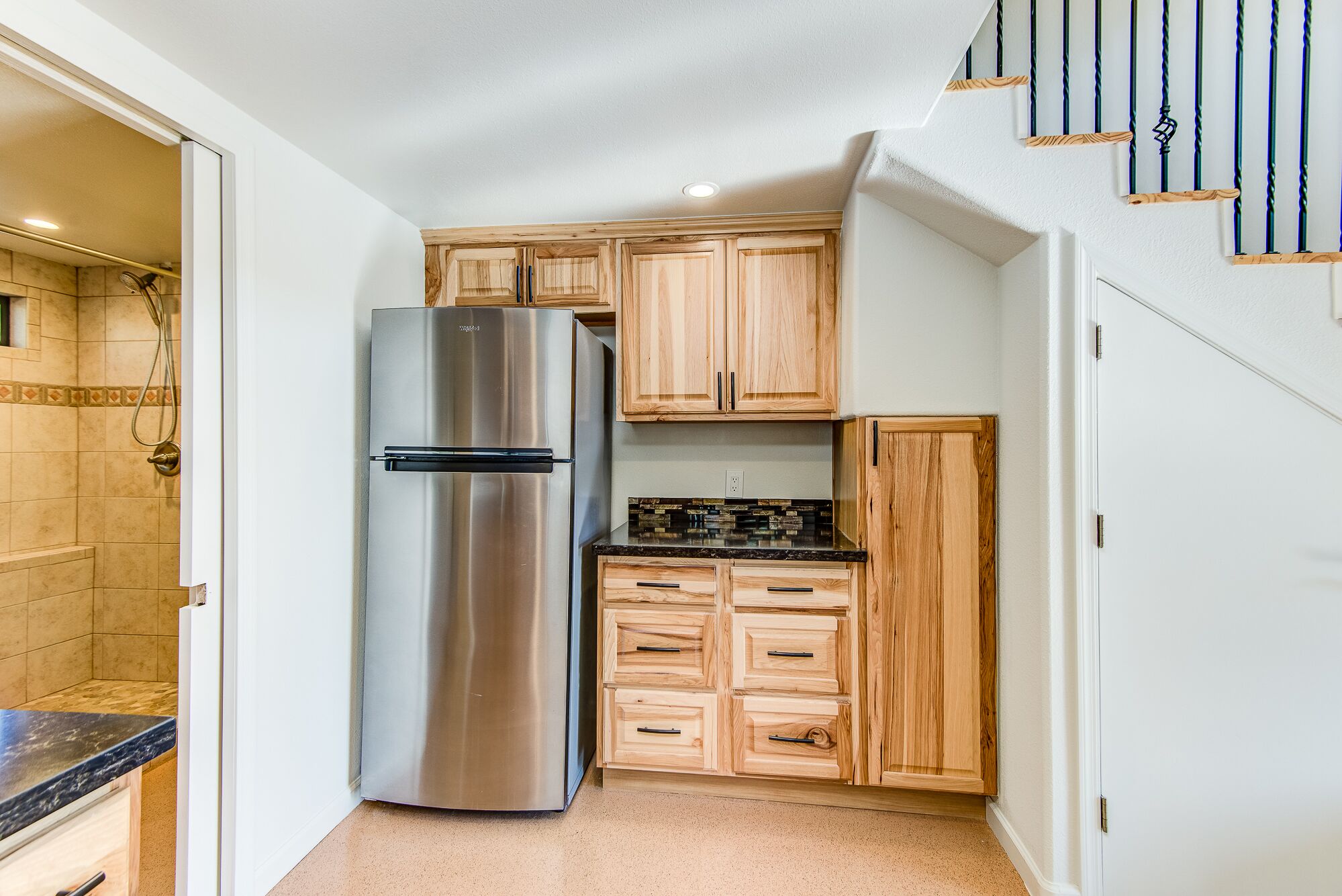 A compact kitchen with a stainless steel refrigerator, wooden cabinets, and a black countertop.