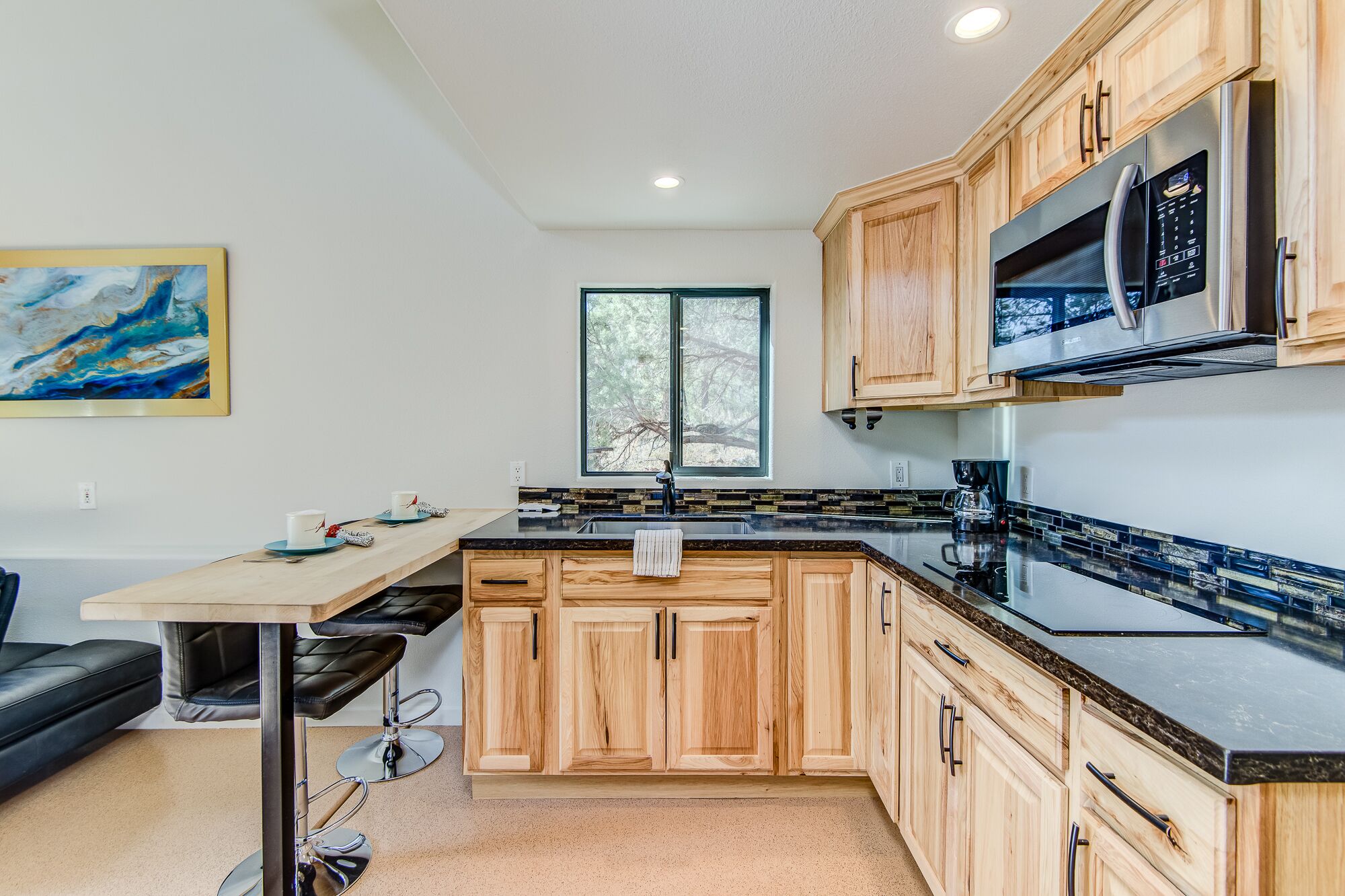 A modern kitchen with wooden cabinets, a black countertop, and a stainless steel refrigerator.