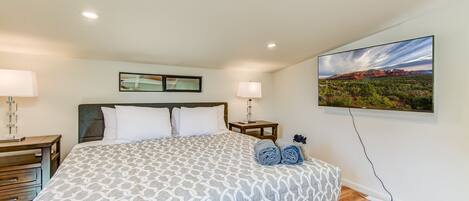 A hotel room with a bed, two bedside tables, a wall-mounted TV, and a painting of a landscape.