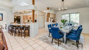 A modern kitchen with a central island, a dining area with blue chairs, and a large window providing natural light. - Sedona Views, Casita, Trail Access (Sedona)