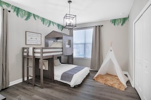 Une chambre d’enfant avec des lits superposés, une tente, une affiche motivante et une fenêtre avec des rideaux.
