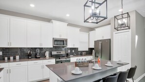 Una cocina moderna con armarios blancos, una isla central con taburetes de bar, un microondas integrado y un refrigerador de acero inoxidable.