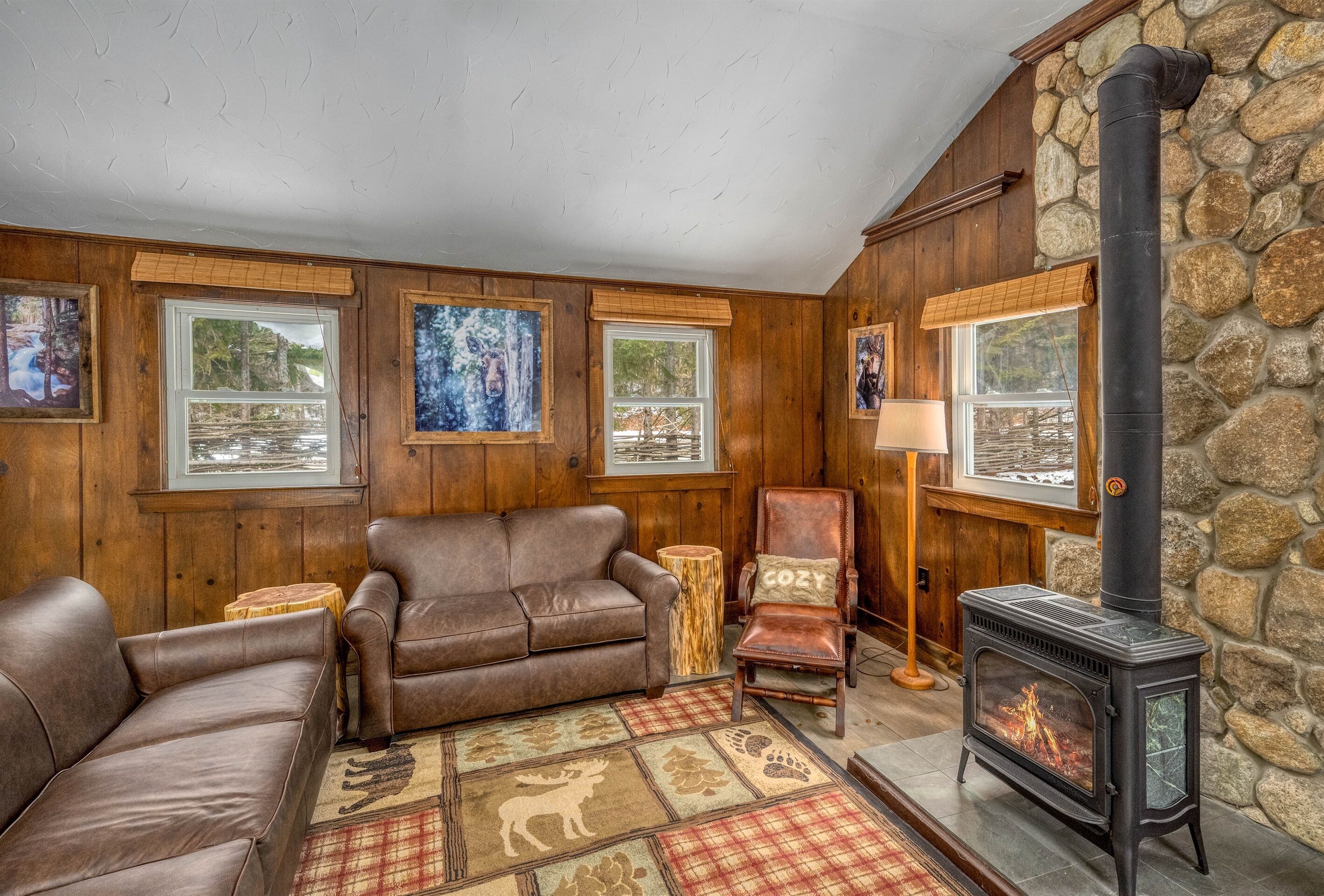 A cozy living room with wooden walls, a stone fireplace, leather sofas, and framed artwork.