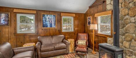 A cozy living room with wooden walls, a stone fireplace, leather sofas, and framed artwork.