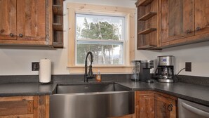 Una cucina con mobili in legno, un lavello in acciaio inox, una finestra vista alberi e una macchina da caffè.