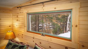 Una stanza accogliente in legno con grandi finestre a cornice verde, una lampada e due cuscini decorati.