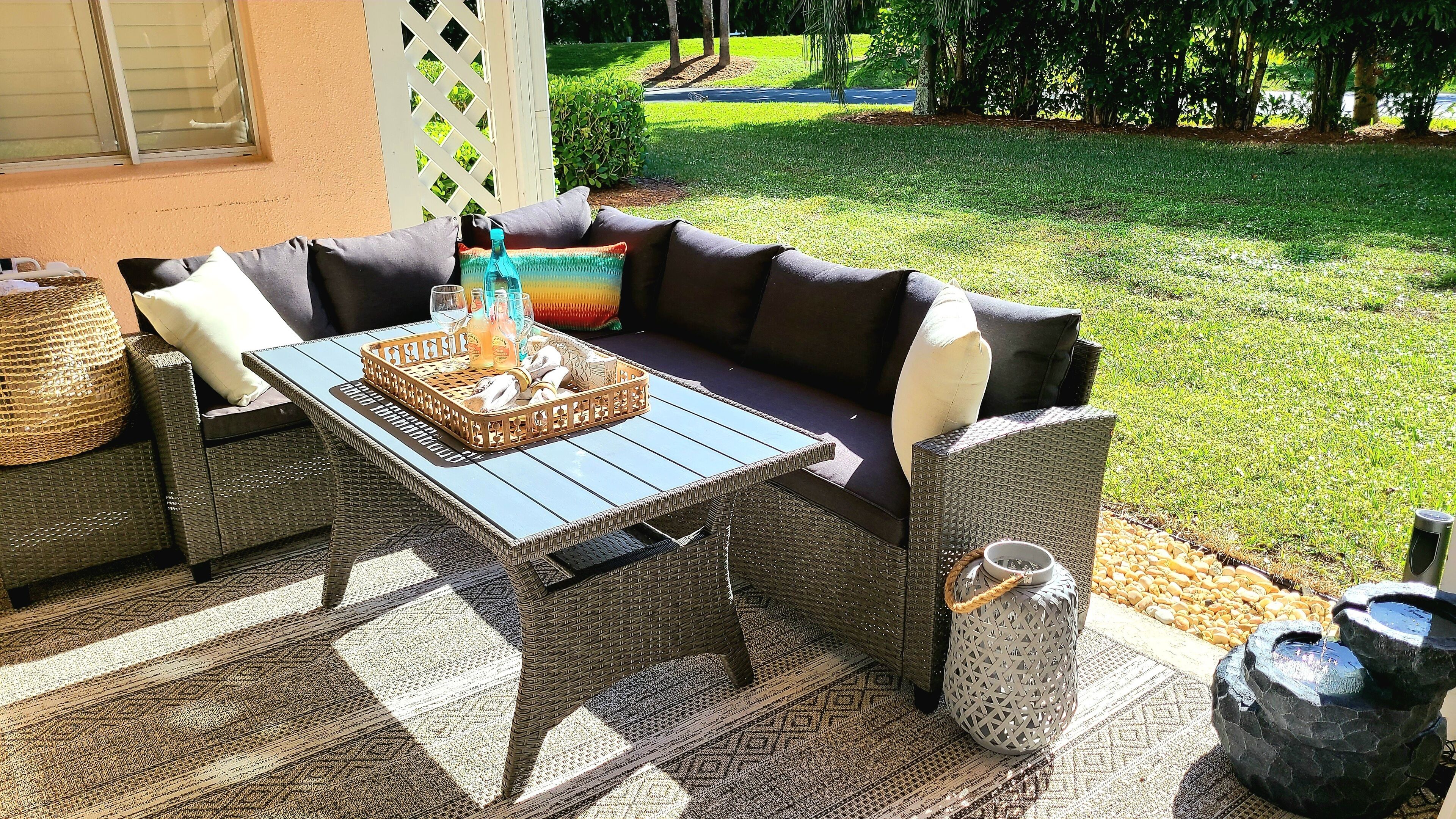 A patio with a wicker sofa, a glass-top table, and a decorative basket.