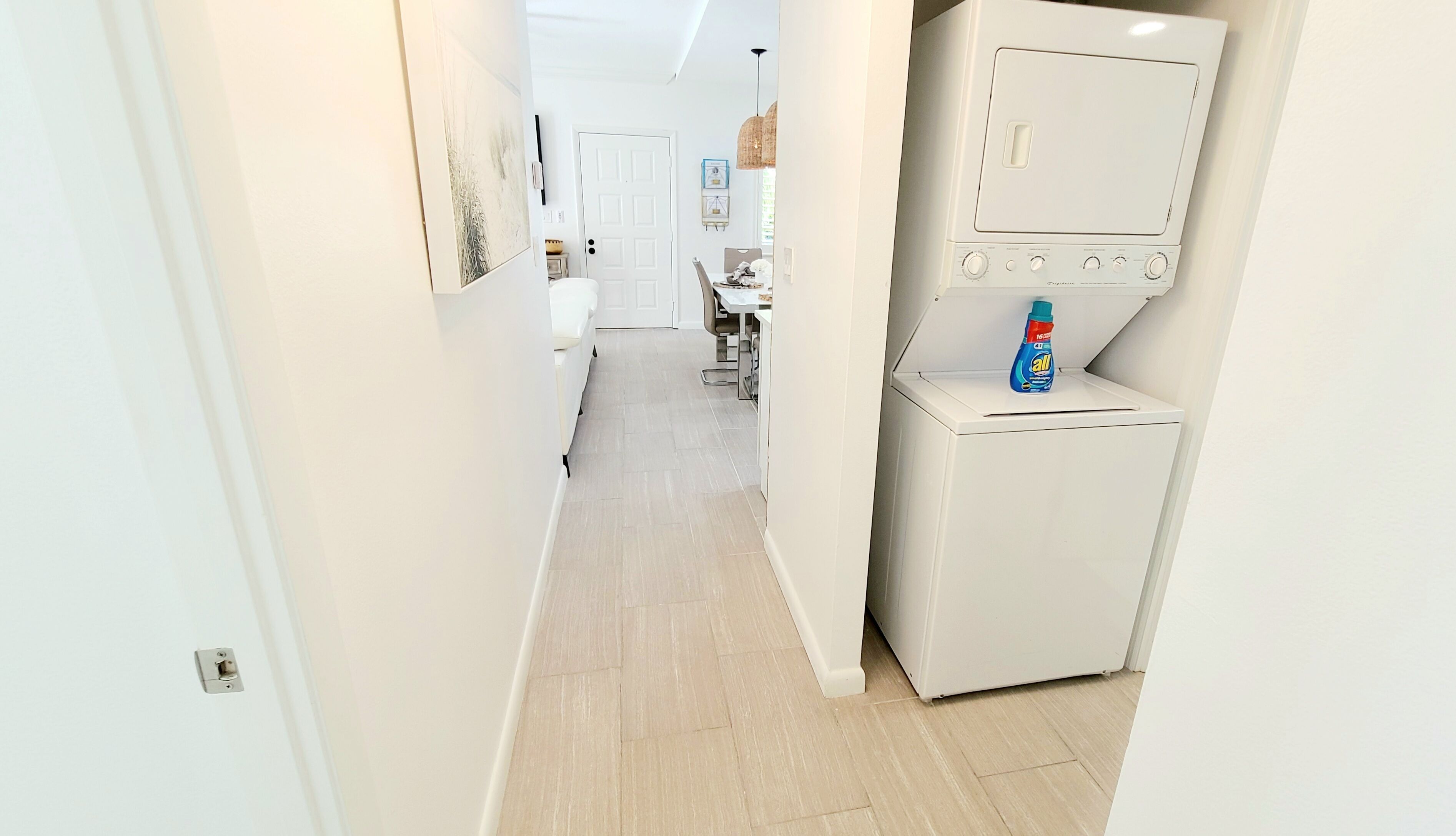 Un couloir avec un lave-linge et une petite table sur laquelle se trouve une bouteille de lessive.