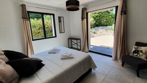 A bedroom with a bed, a chair, a small table, and a view of the outdoors. - La Villa Beau Soleil (Saint-Julien-de-Peyrolas)