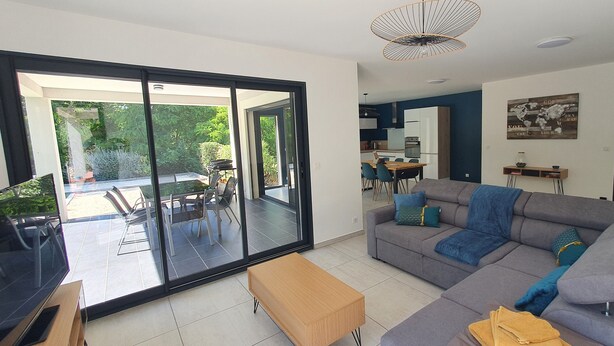 A modern living room with a grey sofa, a wooden coffee table, and a dining area with a table and chairs. - La Villa Beau Soleil (Saint-Julien-de-Peyrolas)