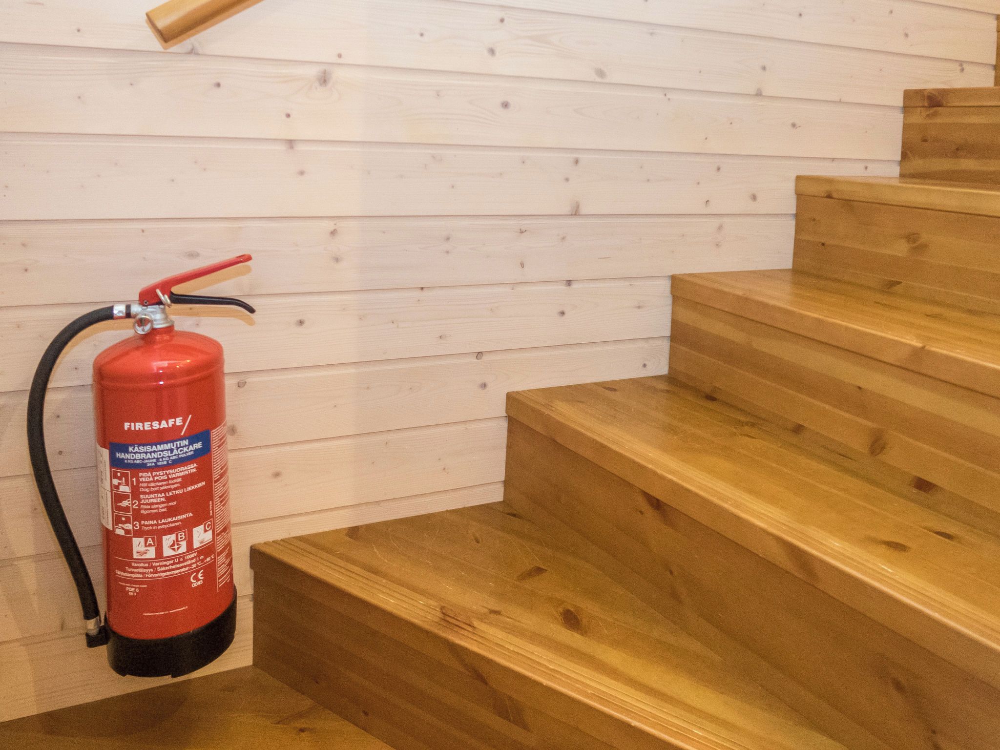 Ein roter Feuerlöscher an einer Holzwand neben einer Holztreppe.