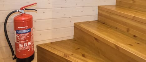 Ein roter Feuerlöscher an einer Holzwand neben einer Holztreppe.
