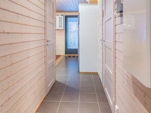 A narrow hallway with wooden walls and a tiled floor, leading to a door with a window.