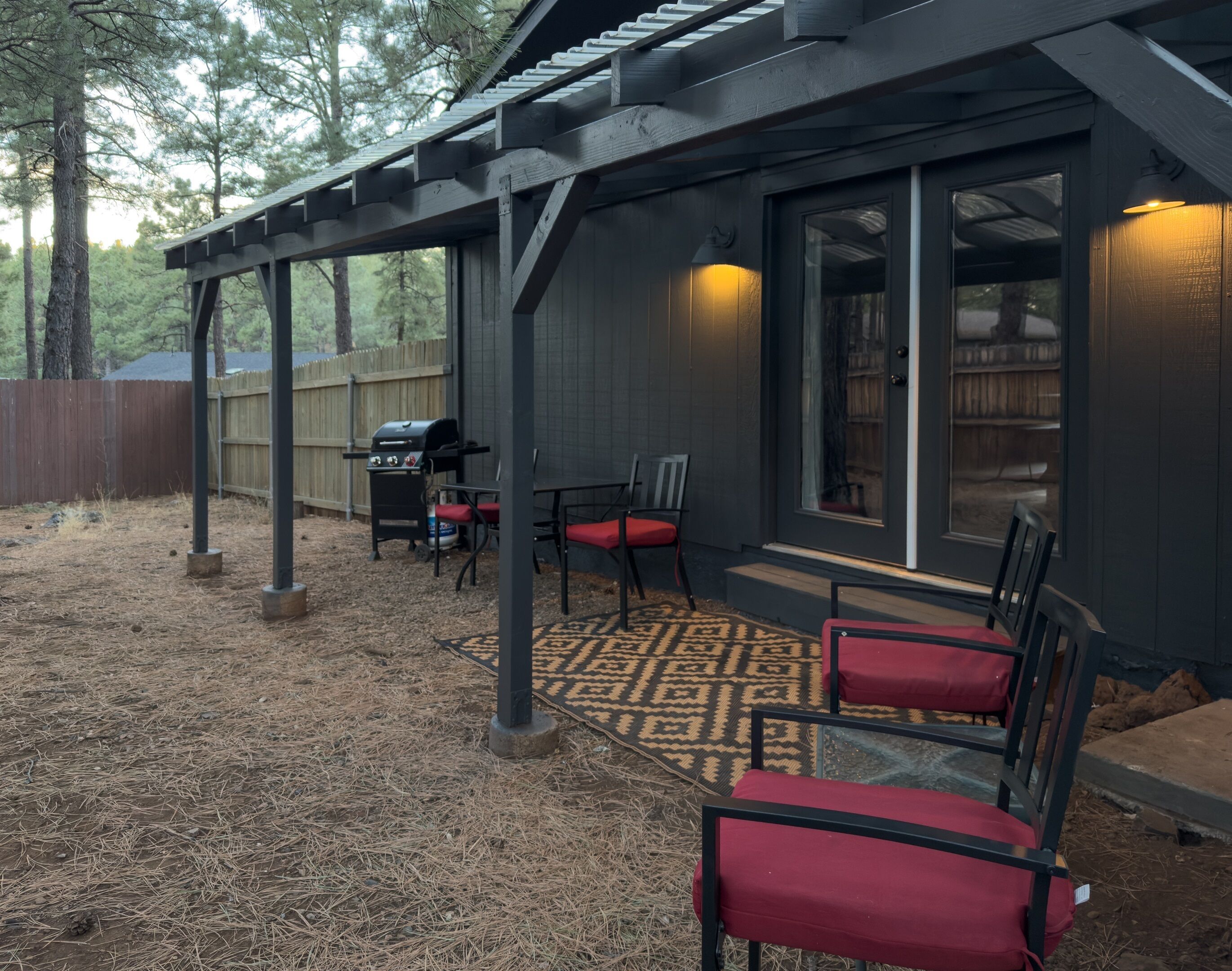 A covered patio area with a grill, chairs, and a patterned rug.