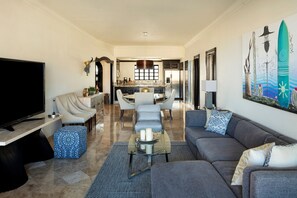 Una sala moderna con un televisor de pantalla plana grande, un sofá, una mesa de centro y un comedor con cocina al fondo.