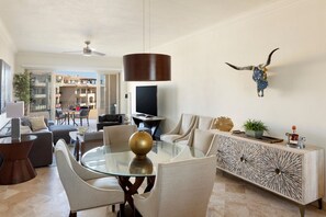 A modern living room with a glass dining table, comfortable seating, a mounted TV, and a decorative bull skull on the wall.