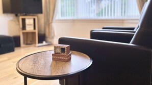 Een moderne woonkamer met een ronde houten tafel, een zwarte leren bank en een flatscreen televisie op een standaard.