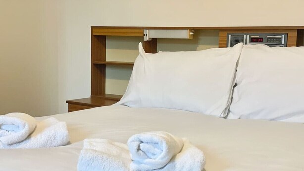 Een net opgemaakt bed met witte lakens en twee opgerolde handdoeken erop.