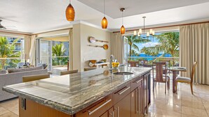 A modern kitchen with a central island, a dining area with a view of the ocean, and a living area with a sofa and a coffee table.