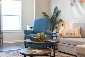 Relax in this inviting living room with a plush armchair, comfortable sofa, and a touch of greenery.