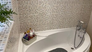 A bathroom with a white bathtub, a shower, and a tiled wall. There is a basket with toiletries on the side of the bathtub. - Ludlow Cozy Apartment Retreat (Ludlow)