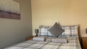 A neatly made bed with a plaid bedspread, two pillows, and two rolled towels. - Ludlow Cozy Apartment Retreat (Ludlow)