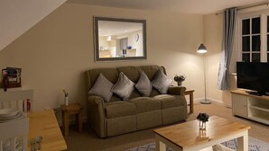 A living room with a sofa, coffee table, and TV. There is a mirror on the wall and a lamp on a side table. - Ludlow Cozy Apartment Retreat (Ludlow)