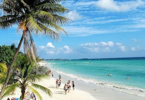 A beach with palm trees, clear turquoise water, and people enjoying the beach.