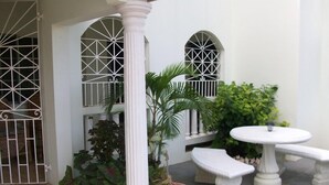 A courtyard with a white column, potted plants, a white table, and a bench. - Apt - Sleeps 5 - Garden - Parking - Balcony (Trelawny)