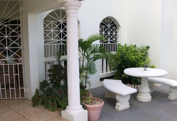 A courtyard with a white column, potted plants, a white table, and a bench.