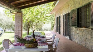 Un patio al aire libre con una mesa dispuesta para comer, rodeado de muros de piedra y contraventanas verdes.