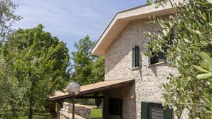 Una casa de piedra con un porche cubierto, contraventanas verdes y un farol.