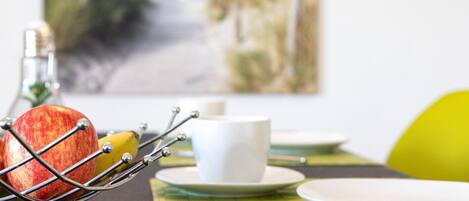 A breakfast setting with a fruit basket, a white cup, and a plate on a table with a woven placemat.