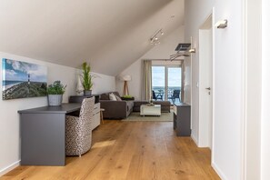 A modern apartment with a loft-style ceiling, a dining area with a table and chairs, a sofa, a small coffee table, and a view of the sea through large windows. - Holiday Apartment "Reeders Topp by Seeblick Ferien" with Harbour View (OstseeResort Olpenitz)