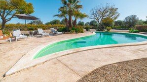 A swimming pool with lounge chairs and umbrellas, surrounded by palm trees and shrubs. - Es Rafalet by Interhome (Llucmajor)