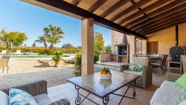A covered outdoor seating area with wicker furniture, a table with fruit, and a stone fireplace. - Es Rafalet by Interhome (Llucmajor)
