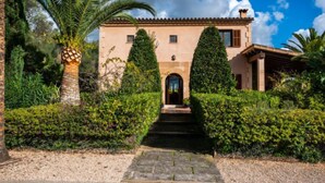 A Mediterranean-style villa with a stone facade, a central entrance, and a well-maintained garden with palm trees and hedges. - Es Rafalet by Interhome (Llucmajor)