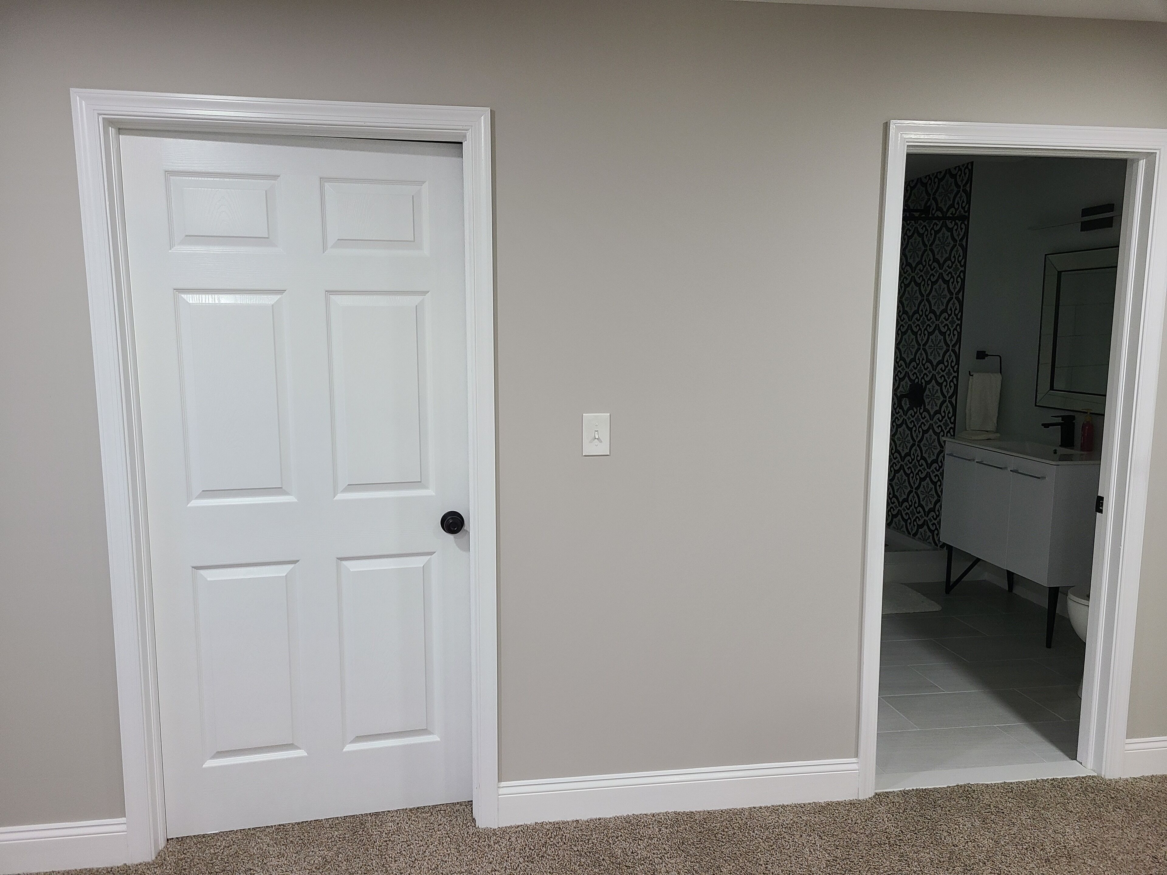 A hallway with a white door and a mirror reflecting a bathroom with a patterned shower curtain.