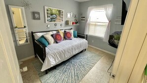 Une chambre à coucher avec un lit, une fenêtre avec des stores, un miroir et des éléments de décoration murale.