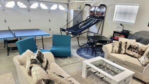 Un salon avec un baby-foot, des chaises bleues, un canapé avec des coussins à motifs et un panier de basket.