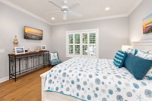 A bedroom with a bed, a desk, a chair, a window, and a ceiling fan.