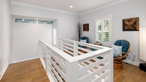 Ein Zimmer mit einem weißen Babybett, einem Korbstuhl und einem Schild an der Wand mit der Aufschrift 'ATLANTIC COTTAGE'.